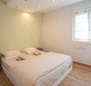 Een slaapkamer met een bed, kussens, een nachtkastje en een raam.