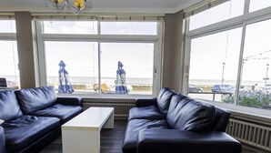 Ein Zimmer mit großem Fenster, einem schwarzen Ledersofa, einem weißen Couchtisch und Blick auf den Strand.