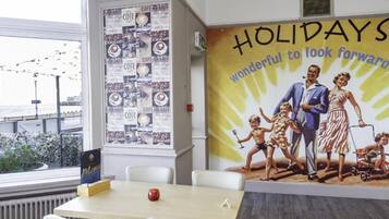Un salón de conferencias con un ventanal amplio, una pared decorada con un cartel de café y un mural que muestra a una familia de vacaciones.
