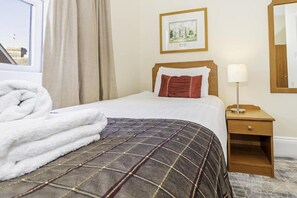 A hotel room with a bed, a bedside table with a lamp, a framed picture on the wall, and a window with curtains. - Majestic Hotel Eastbourne by Belvilla - single sea view (Eastbourne)