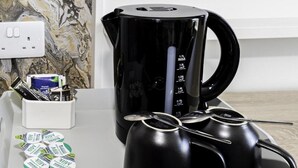 Una zona de cocina con una cafetera negra, tazas medidoras y cartones de leche.