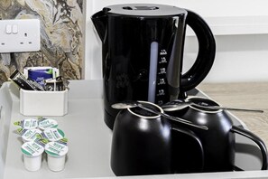 Ett köksutrymme med en svart kaffebryggare, måttsatser och mjölkförpackningar.