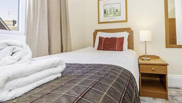 Habitación de hotel con cama, mesita de noche con lámpara, un cuadro enmarcado en la pared y una ventana con cortinas.