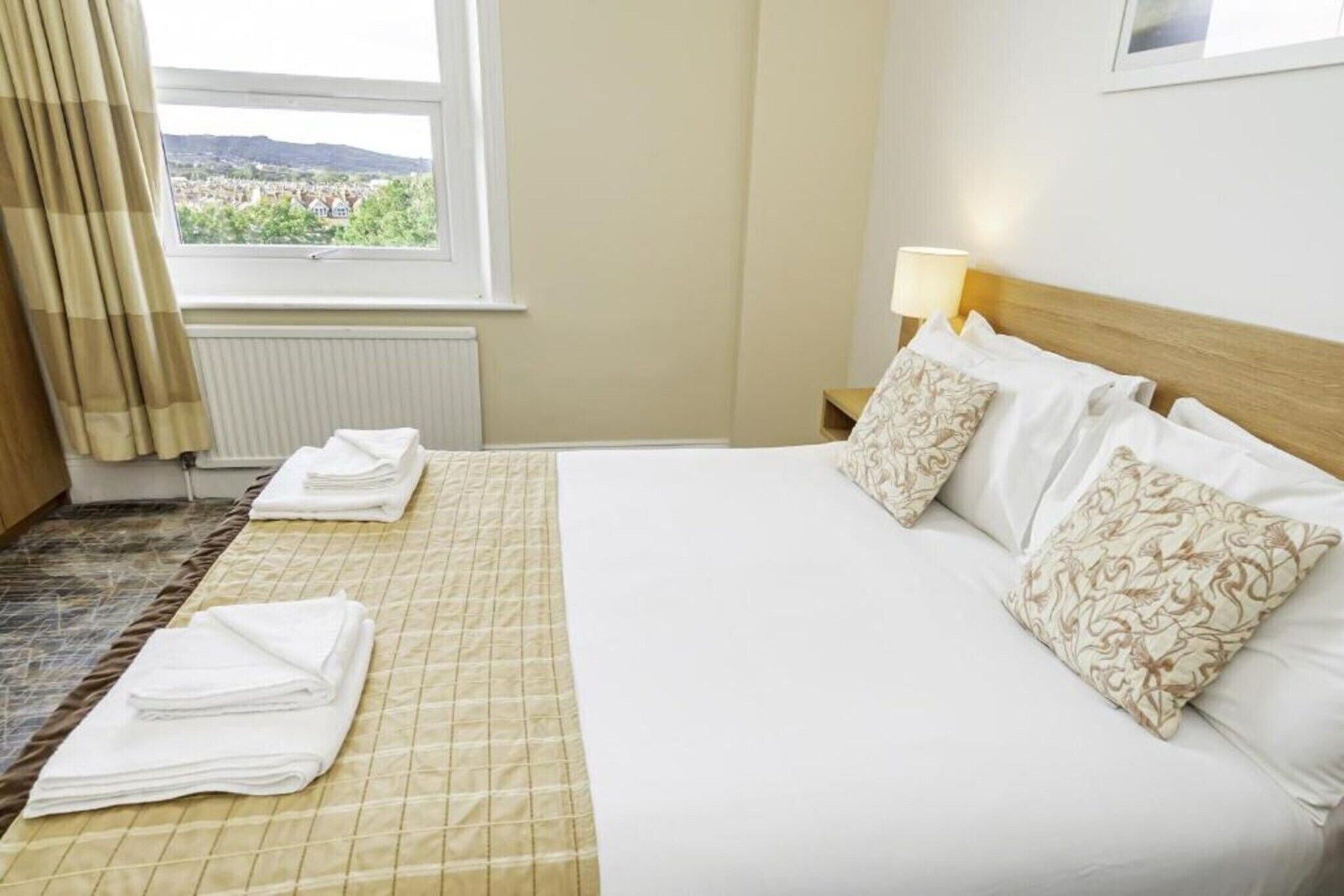 Ein Hotelzimmer mit Bett, Fenster mit Aussicht, Lampe und Heizkörper.