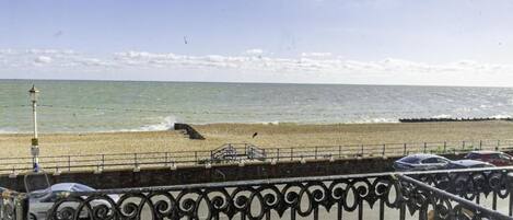 A coastal road with a metal fence, a beach, and the ocean.