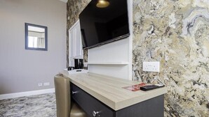 Una habitación con escritorio, silla, televisión y paredes con diseño de mármol.