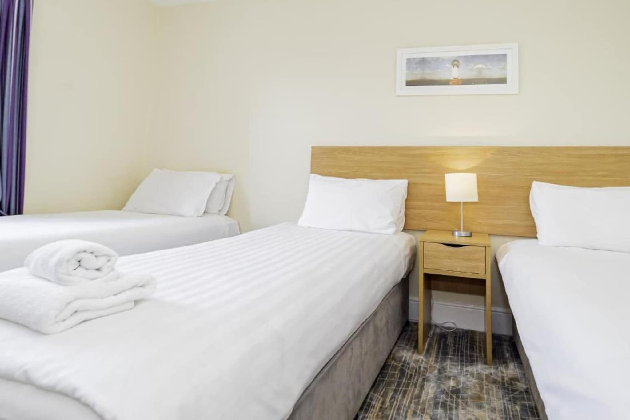 A hotel room with two beds, a nightstand with a lamp, and a painting on the wall.