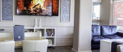 A modern lobby with a fireplace, a flat-screen TV, a sofa, and a bookshelf.