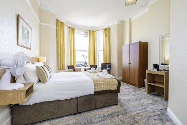 A hotel room with a bed, a desk, a chair, a wardrobe, and a television. - Superior Double Room (Eastbourne)