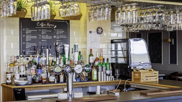 Un espace bar avec un menu de cafés, différentes bouteilles de spiritueux et une tireuse à bière.