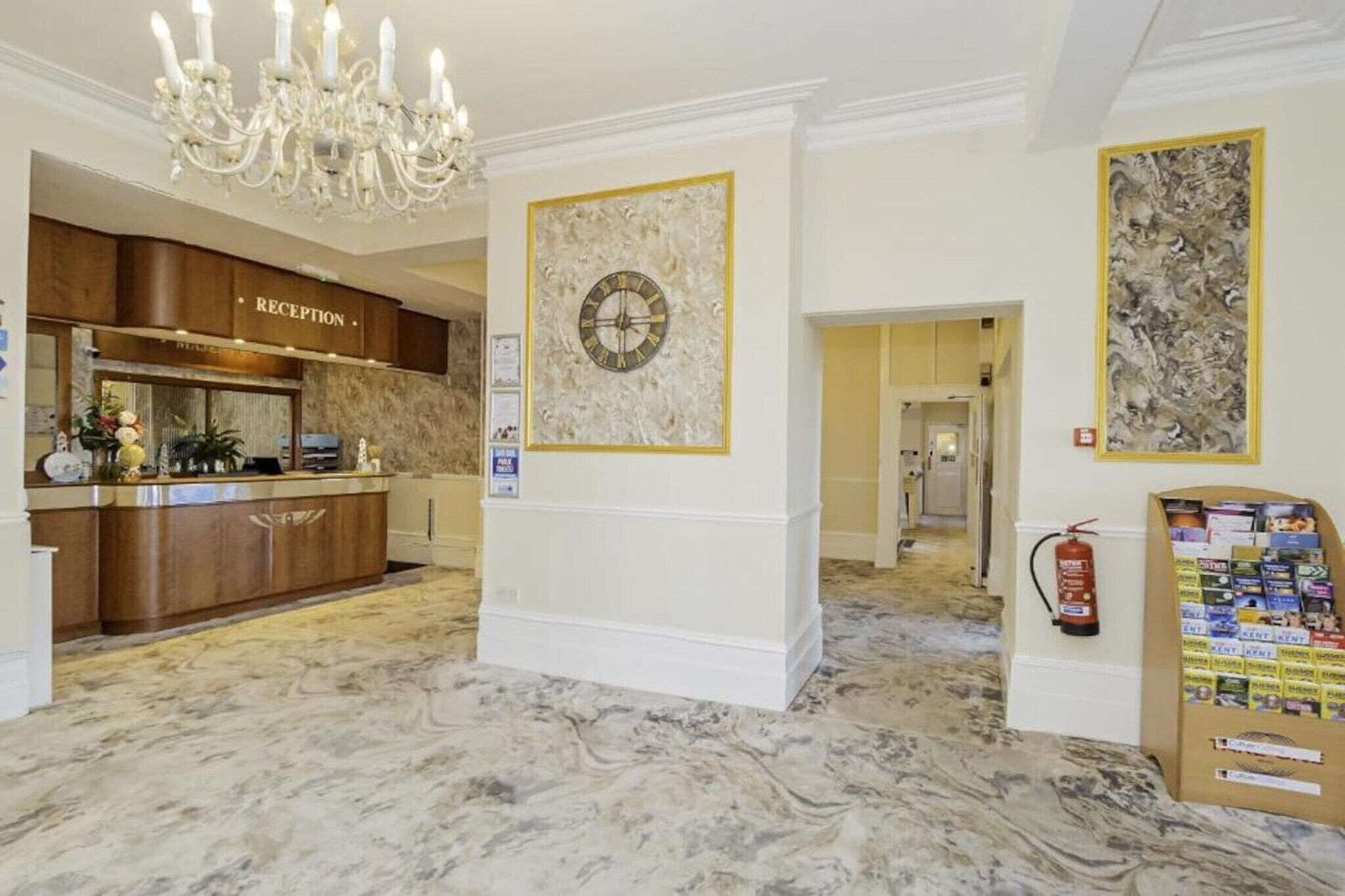 Et receptionsområde med marmorgulv, en lysekrone, en receptionistskranke, et ur og en brandslukker.