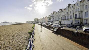 A seaside promenade with a pebble beach, a row of terraced houses, and a pier in the distance.