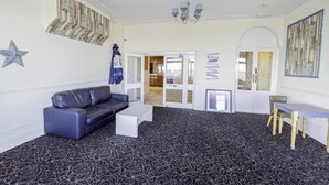 A room with a black patterned carpet, a black leather sofa, a white coffee table, a wooden chair, and a chandelier. - Superior Double Room (Eastbourne)