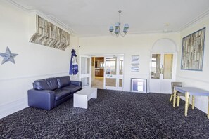 A room with a black patterned carpet, a black leather sofa, a white coffee table, a wooden chair, and a chandelier. - Superior Double Room (Eastbourne)