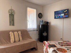 A living room with a sofa, a coffee machine, a kettle, a TV, and a radiator.