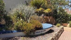 A boat-shaped planter with the name 'Hacienda' on a patio with gravel, surrounded by various plants and trees. - Family apartment with large terrace, swimming pool, parking and wifi fiber (Le Barcarès)