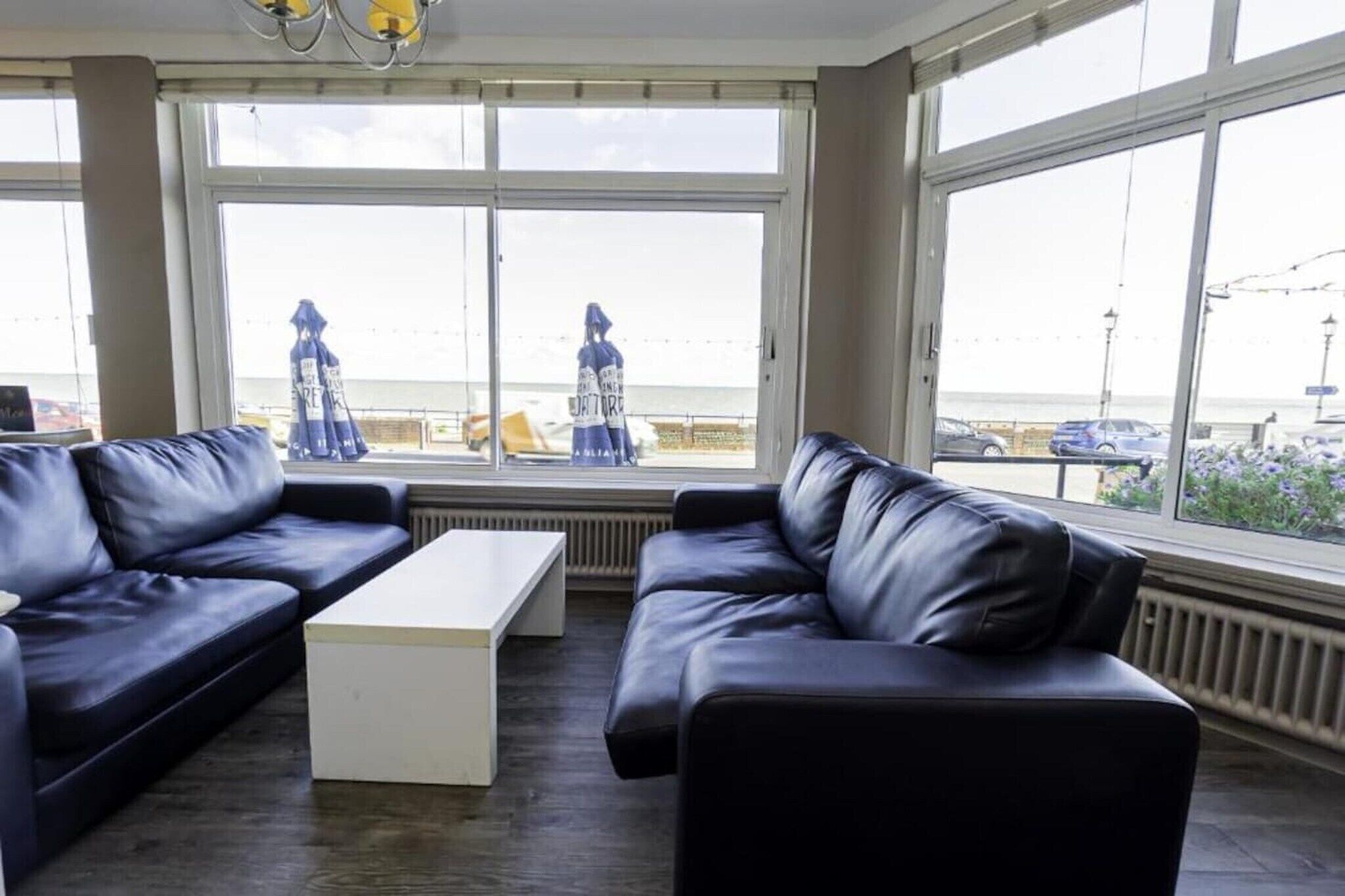 A room with two black leather sofas, a white coffee table, and large windows offering a view of the beach and the sea.