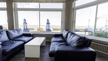 A room with two black leather sofas, a white coffee table, and large windows offering a view of the beach and the sea.