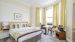 Una habitación de hotel con cama, mesita de noche, ventilador, televisor y vista al mar.