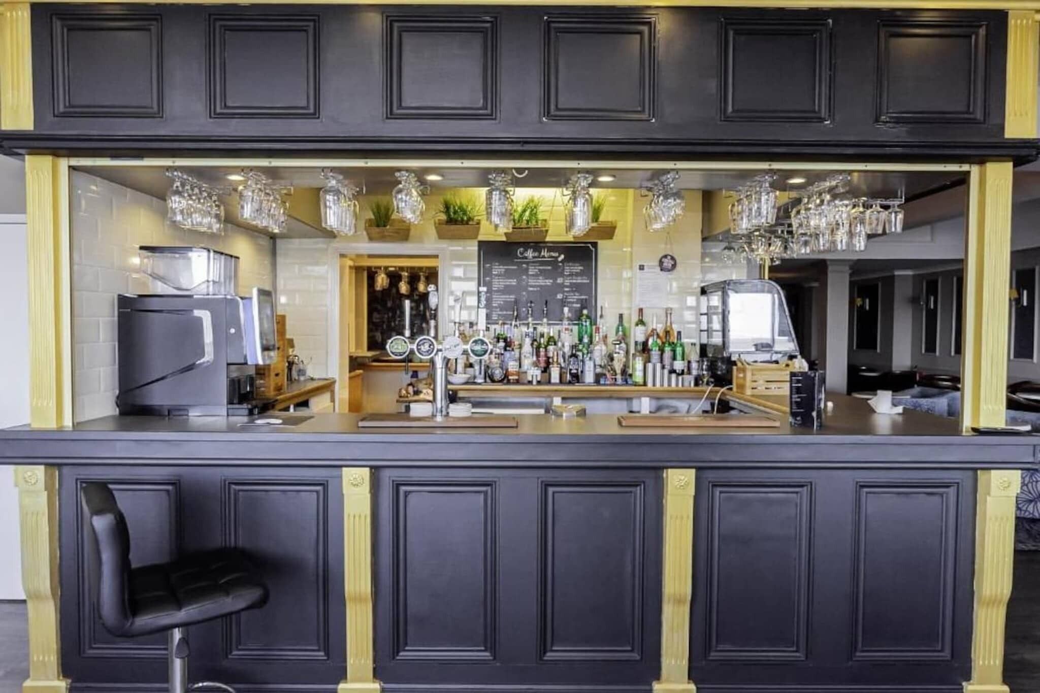 A bar area with a coffee menu, bar stools, and a variety of bottles and glasses.