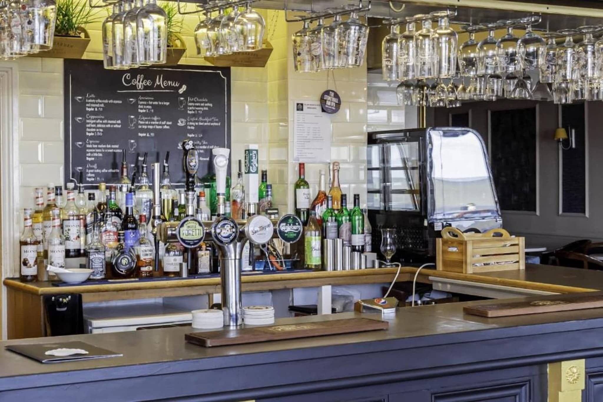 Uma área de bar com cardápio de café, diversas garrafas de bebidas alcoólicas e uma máquina de café.