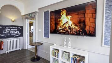 A hotel lobby with a fireplace, a sign for hot drinks, and a bookshelf.