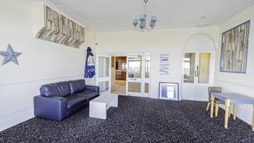 Ein Zimmer mit schwarzem Teppich, einem schwarzen Ledersofa, einem weißen Couchtisch, einem Holzstuhl und einer Chandeliebre.
