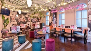 Un acogedor interior de cafetería con mesas, sillas y un mural floral.