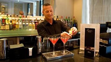 A bartender preparing drinks at a bar with a menu stand and various bottles in the background.