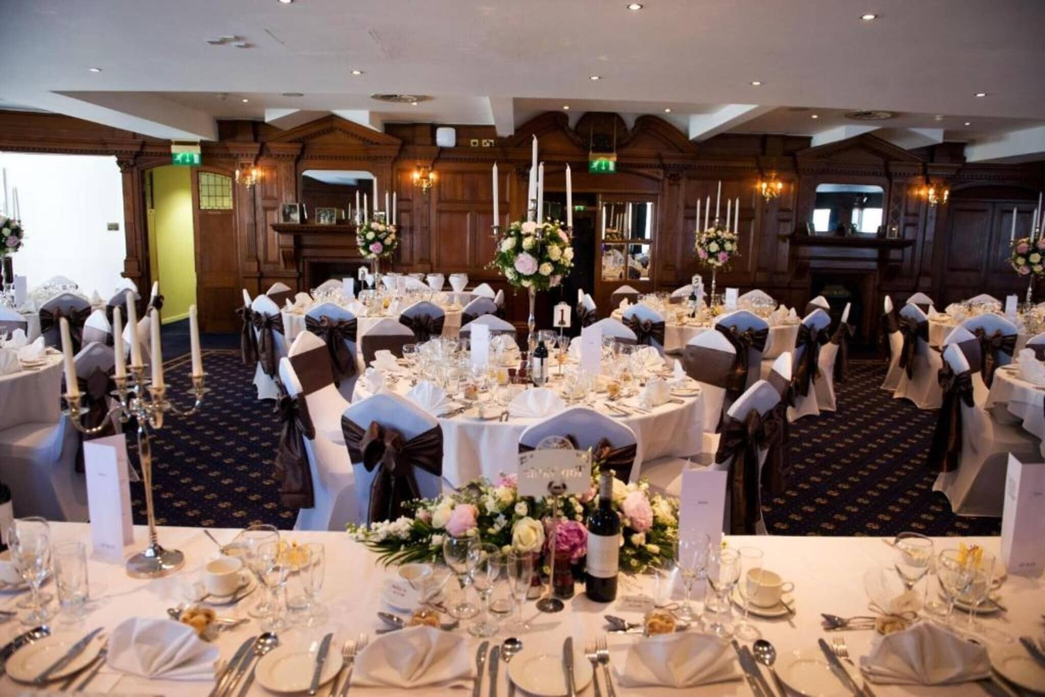 A banquet hall with round tables set for a formal event, featuring white tablecloths, silverware, and floral centerpieces.