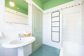 A bathroom with a white sink, a door, a towel rack, and a bathtub.