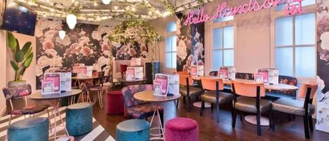 A cozy cafe interior with tables, chairs, and a floral wall mural.