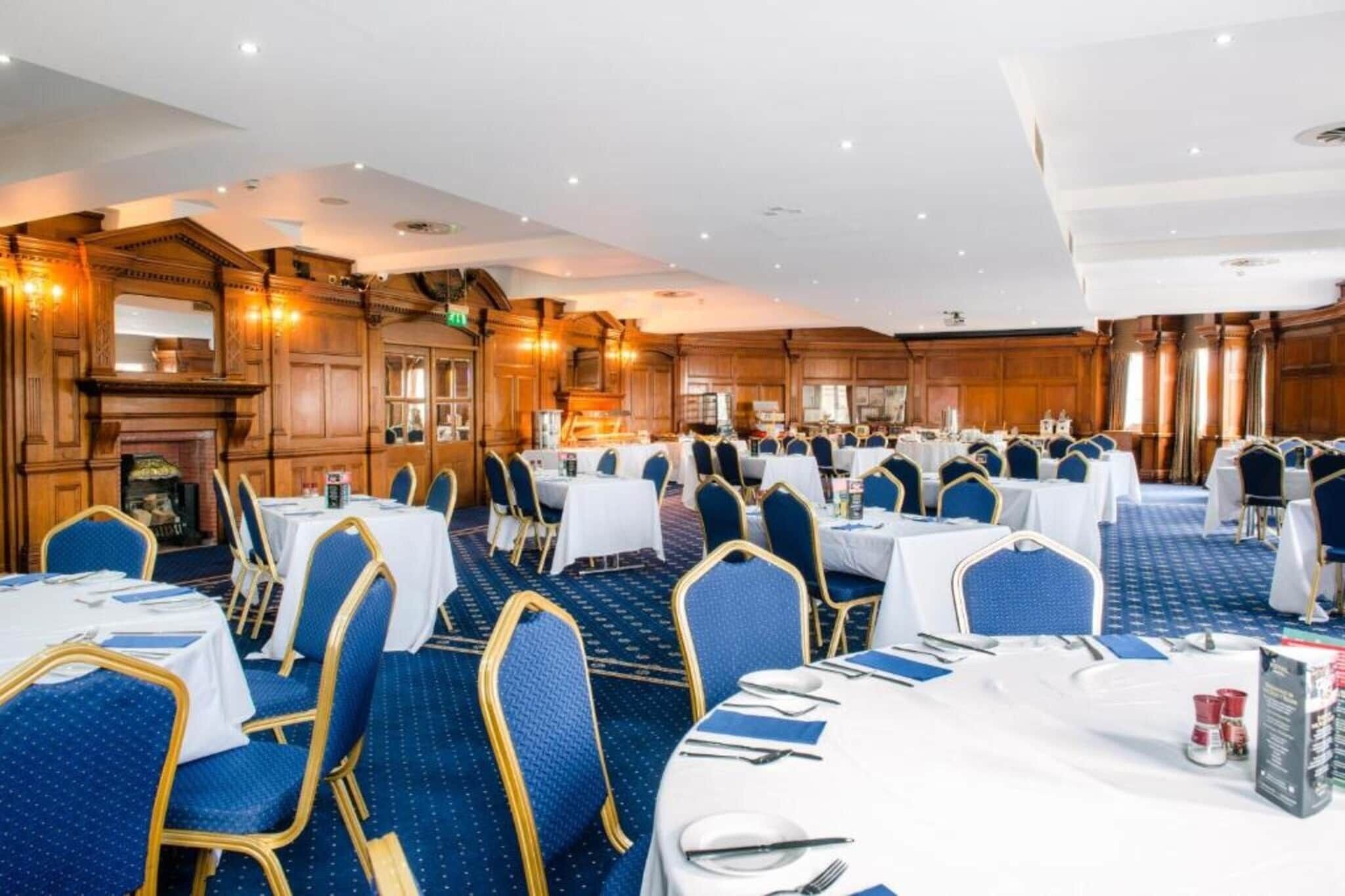 A banquet hall with multiple round tables, blue upholstered chairs, and a classic wooden interior.