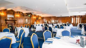 A banquet hall with multiple round tables, blue upholstered chairs, and a classic wooden interior.