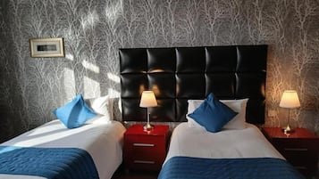 A hotel room with two beds, a dark headboard, bedside lamps, and a patterned wallpaper.