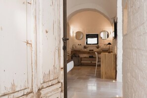 Ein rustikales Interieur mit einer weißen Tür, einem Kachelboden, einer Holzbank und einem Spiegel an der Wand.