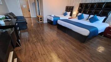 Una habitación de hotel con piso de madera, dos camas con cabeceras, un escritorio y una silla.