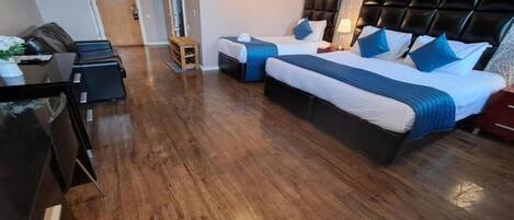 A hotel room with a wooden floor, two beds with headboards, a desk, and a chair.