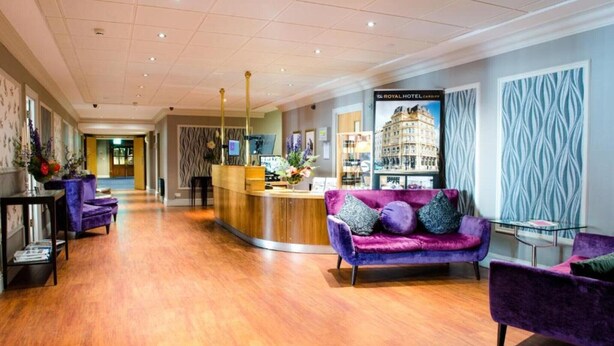 Un hall d’hôtel avec un comptoir d’accueil, un canapé violet et un plancher en bois.