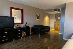 Ein Hotelzimmer mit Flachbildfernseher, Schreibtisch mit Schubladen, schwarzem Ledersofa und Bett.