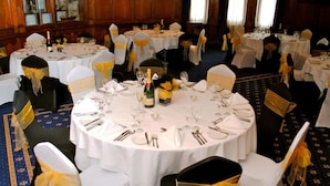 A banquet hall with round tables set for dining, each with white tablecloths and chairs with yellow sashes. - Royal Hotel Cardiff by Belvilla - Standard Double Room - No Window (Cardiff)