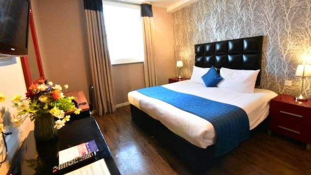A hotel room with a bed, a nightstand, a TV, a vase with flowers, and a window with curtains. - Royal Hotel Cardiff by Belvilla - Standard Double Room - No Window (Cardiff)