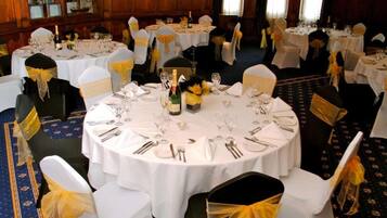 A banquet hall with round tables set for dining, each with white tablecloths and chairs with yellow sashes.
