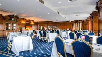 A banquet hall with round tables, blue upholstered chairs, and a patterned carpet.
