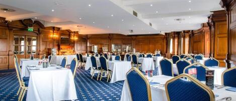 A banquet hall with round tables, blue upholstered chairs, and a patterned carpet.