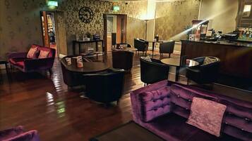 A hotel lobby with a purple sofa, multiple chairs, a coffee bar, and a patterned wall.