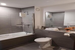 Une salle de bain moderne équipée d’une baignoire, de toilettes et d’une douche séparée par des parois en verre.