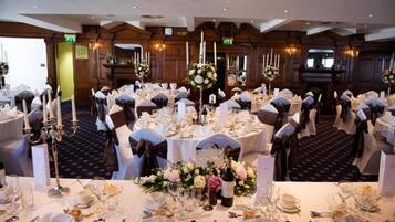 A banquet hall with round tables set for a formal event, featuring white tablecloths, silverware, and floral centerpieces.