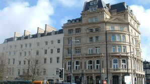 Ein mehrstöckiges Gebäude mit klassischer Architektur, ein Hauseingang an einer Ecke und zahlreiche Fenster.