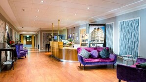 Eine Hotelhalle mit Rezeption, violetten Sofas, Holzboden und einer Wand mit Muster.